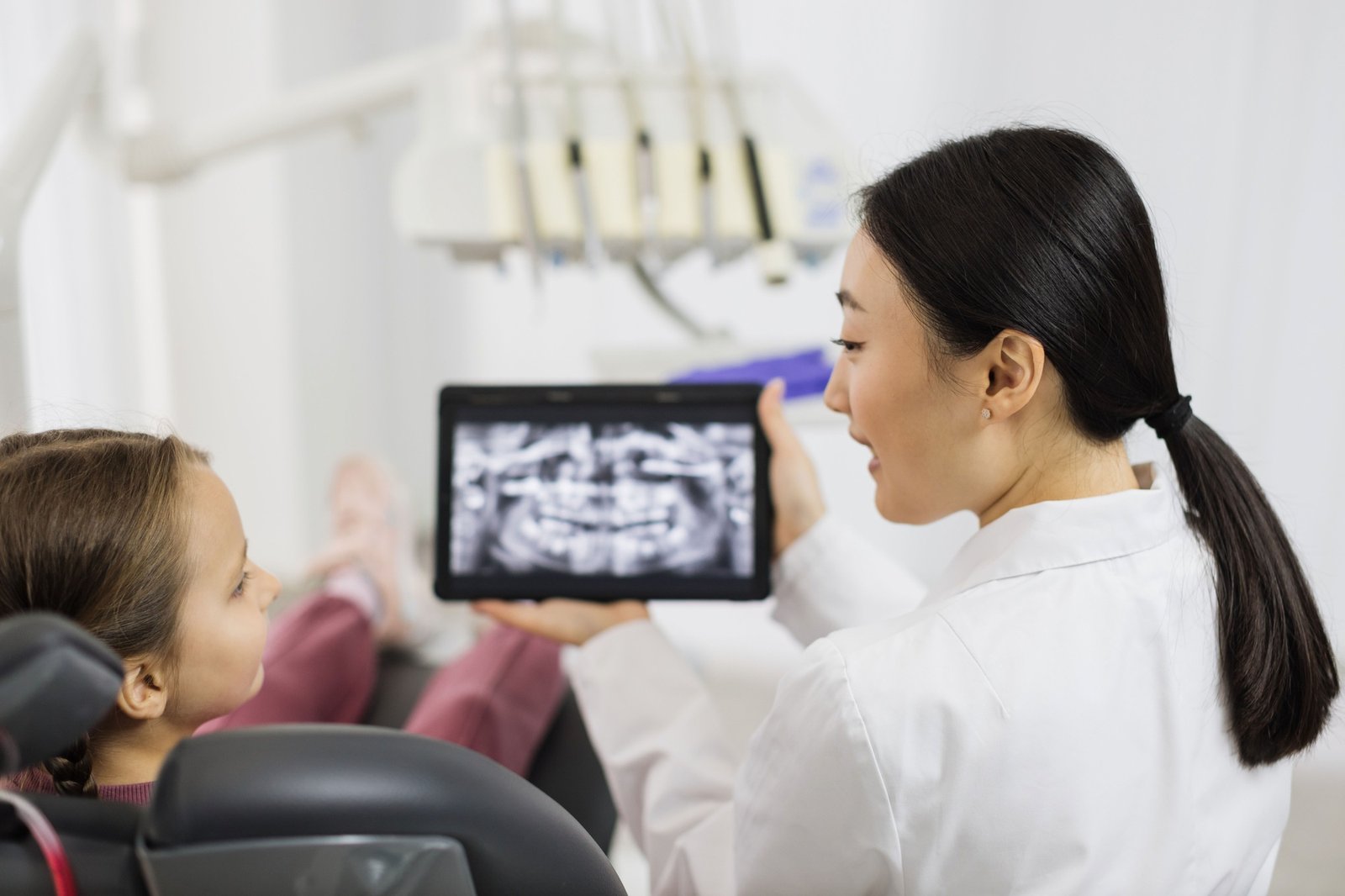 Back view of smiling happy caucasian child girl visiting dentist, sitting in dental chair