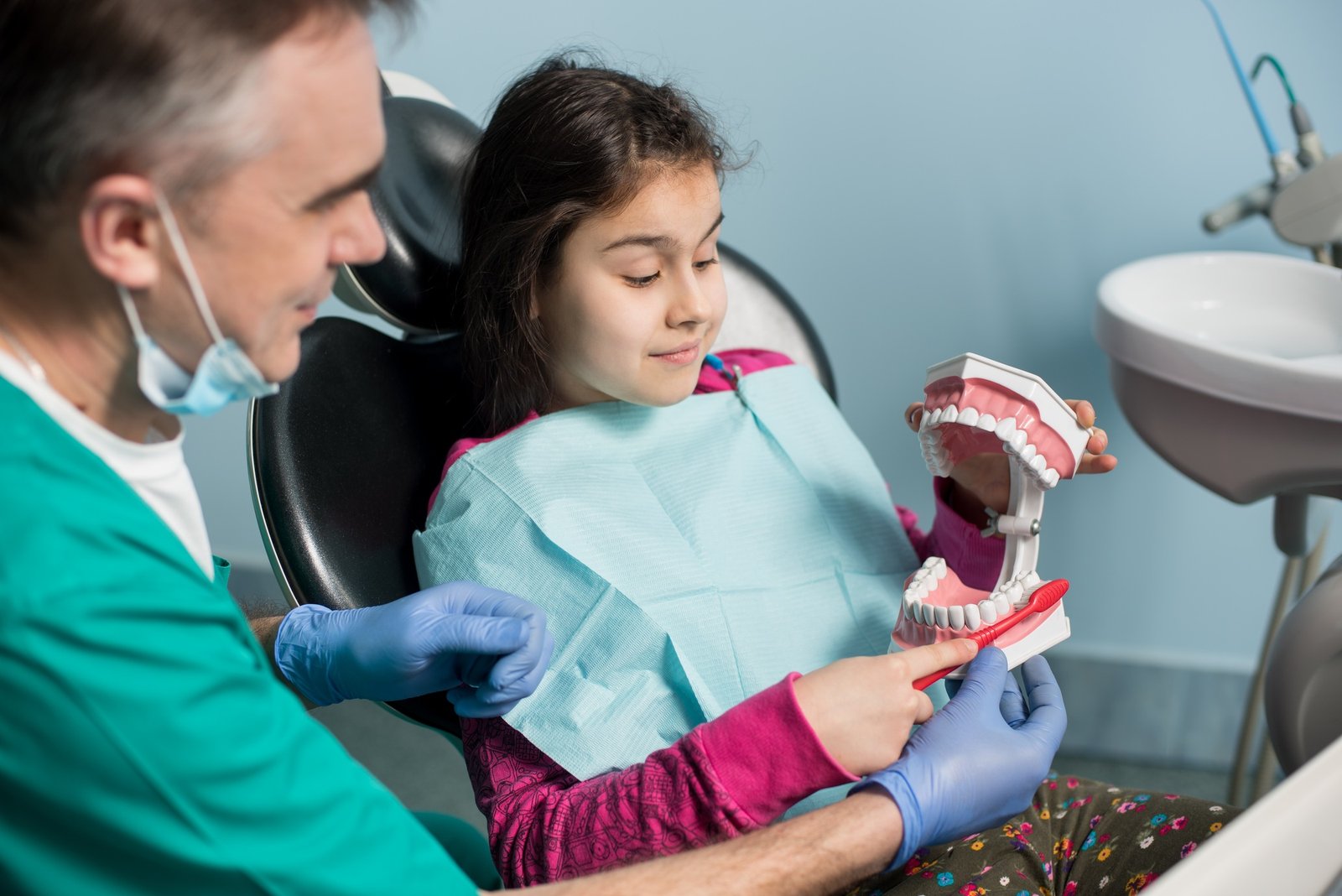 Girl with on the first dental visit. Senior pediatric dentist treating patient teeth